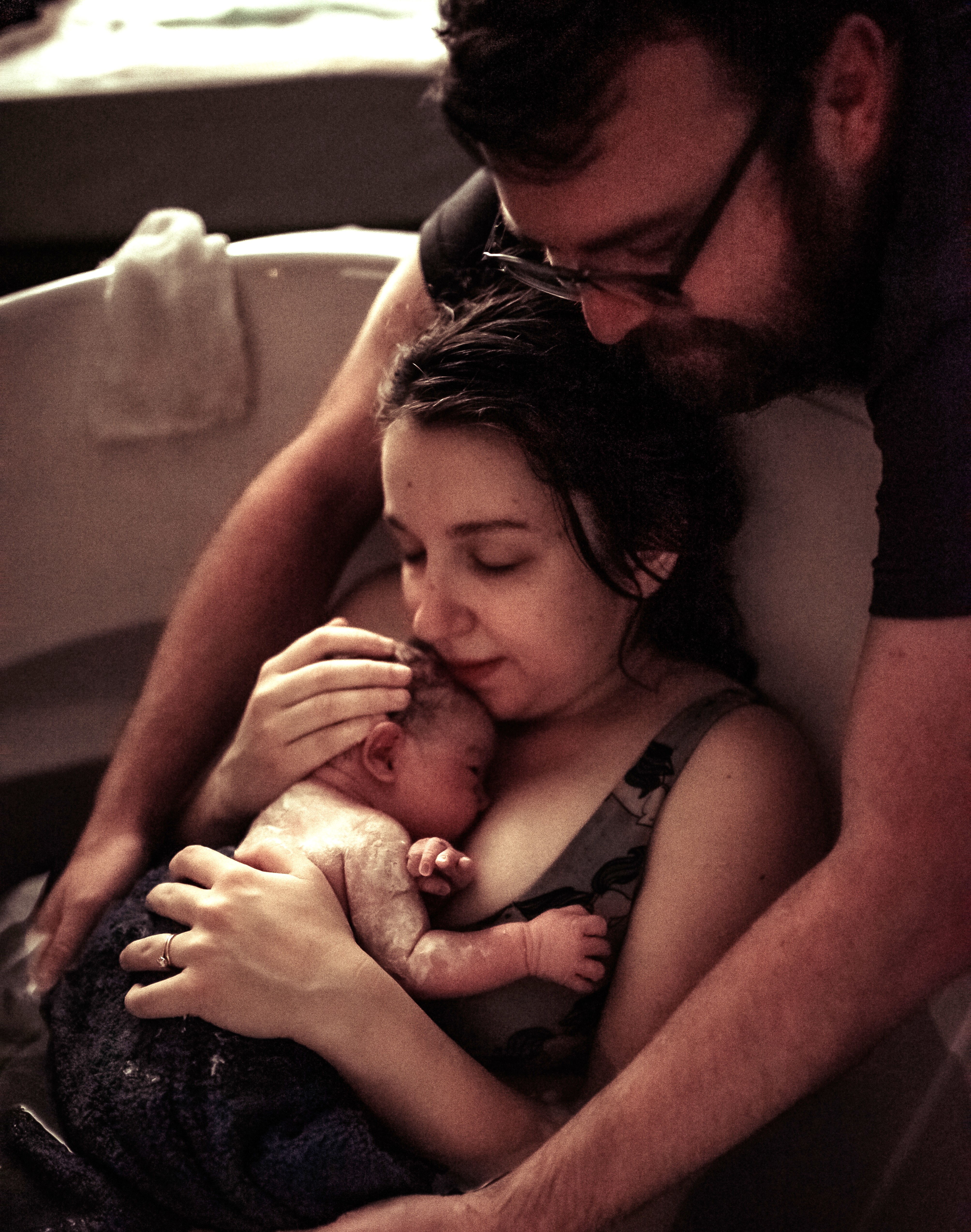 Woman holding newborn with husband surrounding both, right after giving birth