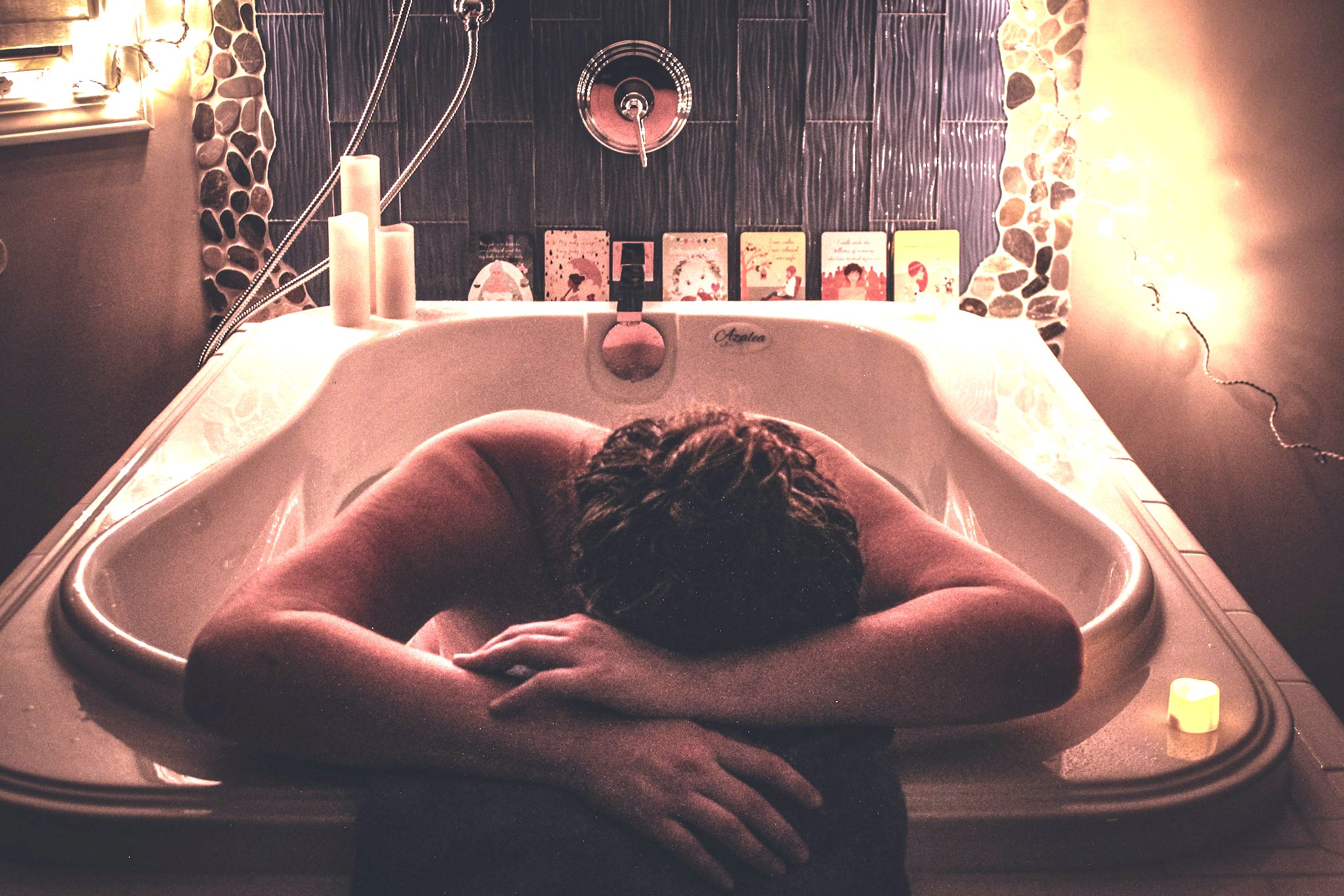 Woman resting in tub while in labor, with affirmation and low lights.